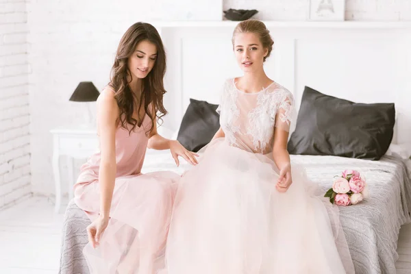 Delighted bride and bridesmaid sitting in the white room — Stock Photo, Image