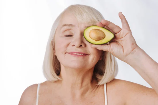 Kvinna som håller en avokado hälften nära ögat — Stockfoto
