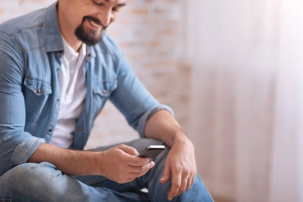 Encantado hombre barbudo sentado y sosteniendo el teléfono — Foto de Stock