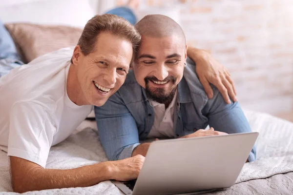 Positivo gay casal deitado no o cama e assistindo filme — Fotografia de Stock