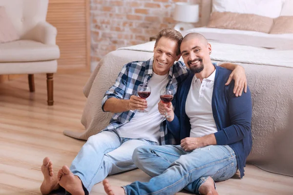 Sonriente pareja homosexual bebiendo vino en el dormitorio — Foto de Stock