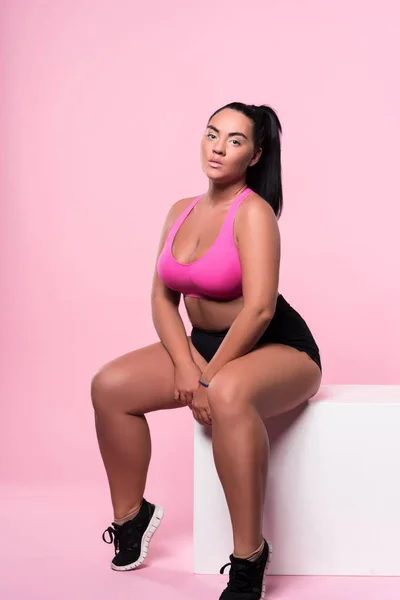 Sexig knubbig mulatt kvinna sitter på rosa bakgrund — Stockfoto