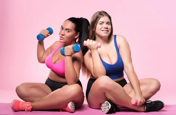 Two plump women posing with dumbbells on floor — Stock Photo, Image