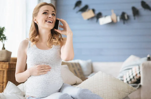 Захоплена вагітна жінка говорить на мобільному телефоні в ліжку — стокове фото