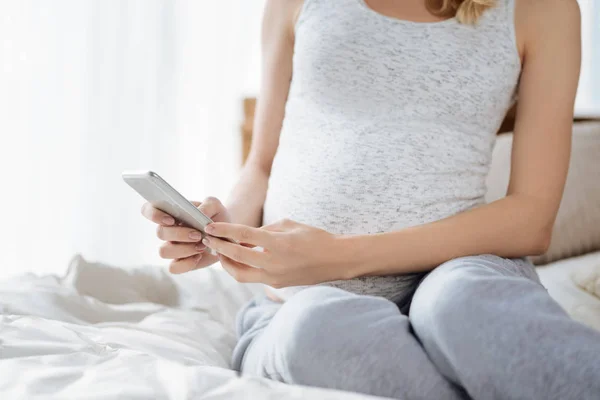 Крупним планом вагітна жінка використовує смартфон у спальні — стокове фото