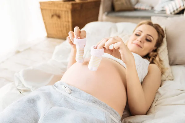 Pregnant woman holding baby socks in bed — Stock Photo, Image