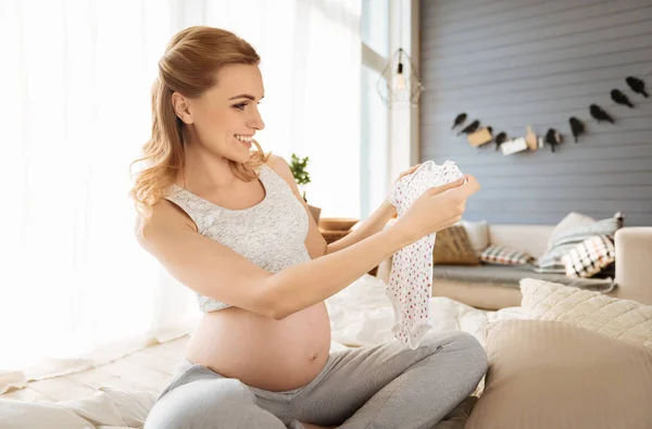 Pregnant woman holding baby clothes — Stock Photo, Image