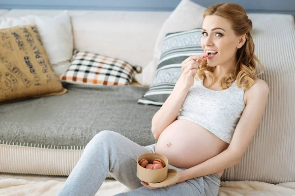 Pregnant joyful woman eating macaroons — Stock Photo, Image