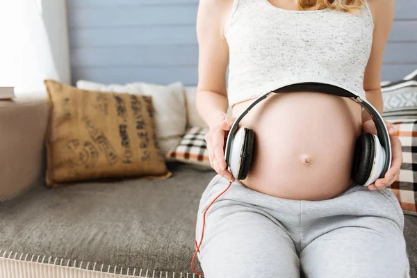 Close up of pregnant woman using headphones on her belly — Stock Photo, Image