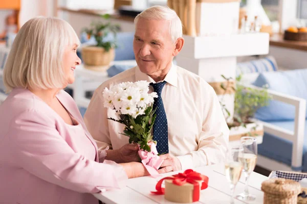 Gallant grey haired man presenting his lady flowers — Stock Photo, Image
