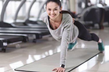 Gülümseyen kız bir spor salonunda egzersizleri yapıyor.