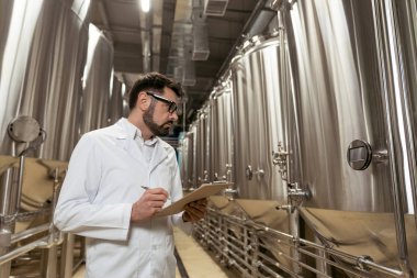 Bira fabrikasında notlar alan konsantre bir adam.