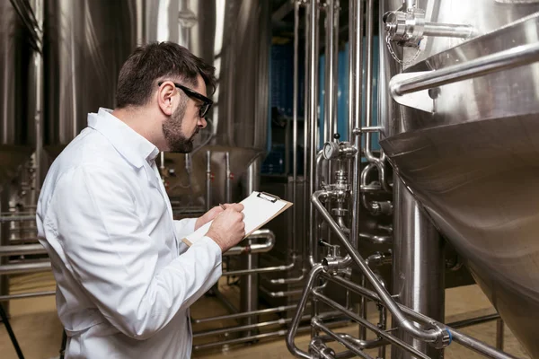 Homem concentrado a fazer anotações na fábrica de cerveja — Fotografia de Stock