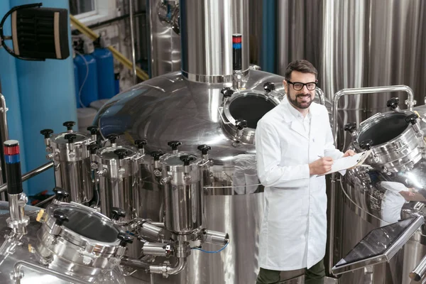 Lächelnder Mann kontrolliert Mechanismen in Bierfabrik — Stockfoto