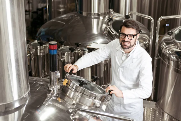 Улыбающийся человек с помощью пивоваренного механизма на заводе — стоковое фото
