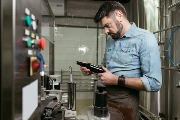 Serious man discovering a bottle of alcohol at brewery — Stock Photo, Image