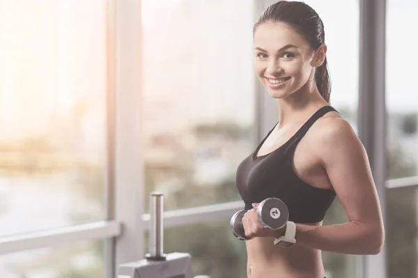 Mujer sonriente sosteniendo las mancuernas en el gimnasio — Foto de Stock