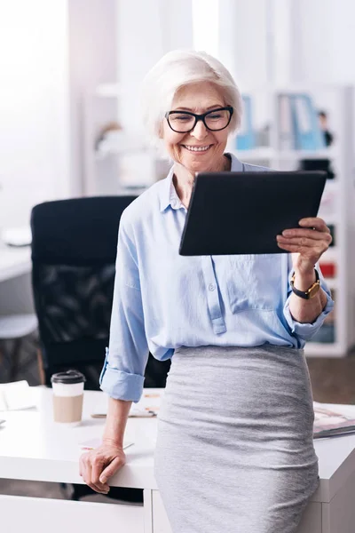 Charmante femme d'affaires âgée positive bénéficiant d'un nouveau gadget dans le bureau — Photo