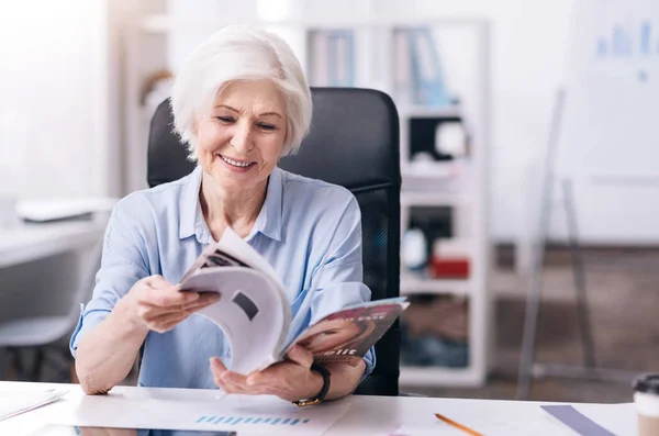 Una anciana empresaria sonriente leyendo la revista en la oficina — Foto de Stock