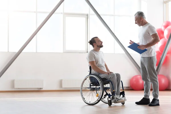 Sourire jeune patient handicapé ayant une conversation avec son physiothérapeute — Photo