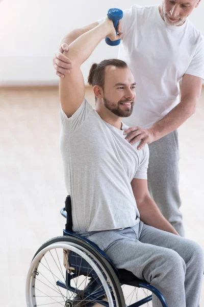 Hombre discapacitado encantado haciendo ejercicio con su asistente en el gimnasio — Foto de Stock