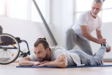 Aged bearded father stretching his disabled son in the gym clipart
