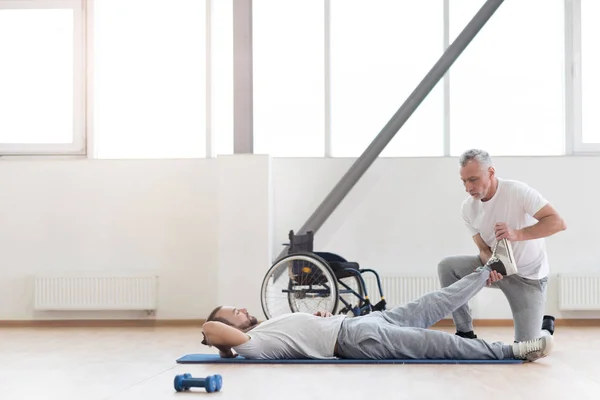 Ortopedista experto haciendo ejercicio con un paciente discapacitado en el gimnasio — Foto de Stock