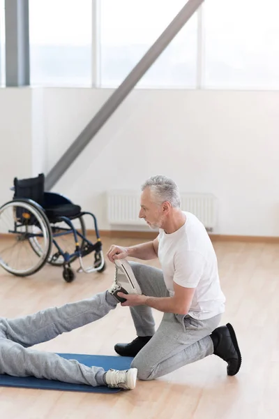 Uppmärksamma äldre ortoped hjälpa funktionshindrade patienten i gymmet — Stockfoto