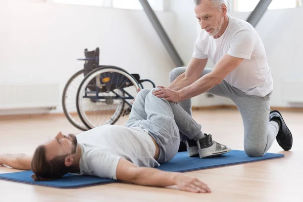 Proficient general practitioner stretching the disabled in the gym — Stock Photo, Image