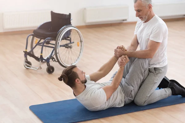 Ortopedista idoso forte ajudando os deficientes no ginásio — Fotografia de Stock