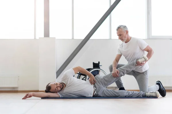 Involved physical therapist stretching the handicapped in the gym — Stock Photo, Image