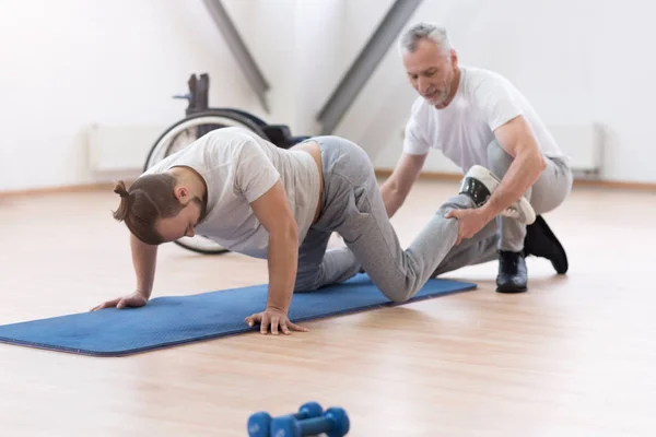 Věku fyzioterapeuta táhnoucí postižené v tělocvičně — Stock fotografie