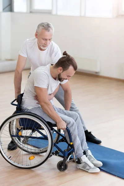 Helpful bearded father helping his disabled son in the gym