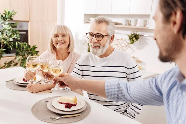 Smiling elderly couple relishing dinner with their child at home — Stock Photo, Image