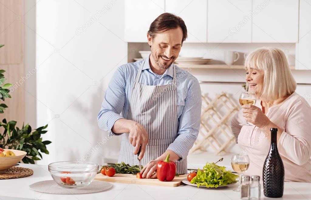Skillful son helping aged mother in the kitchen