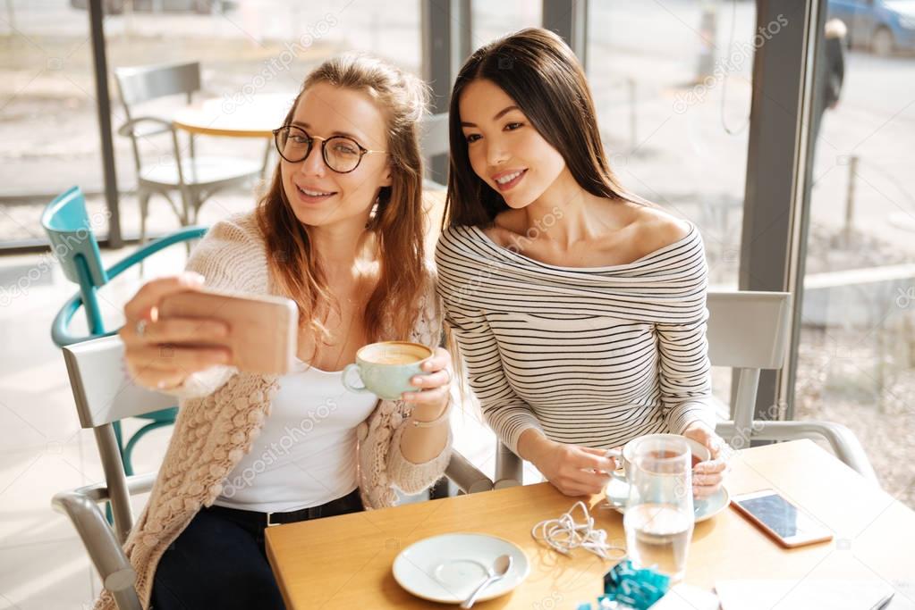 Two girlfriends making selfies in the cafe
