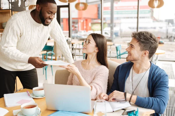 Joven dando papeles a sus compañeros estudiantes — Foto de Stock