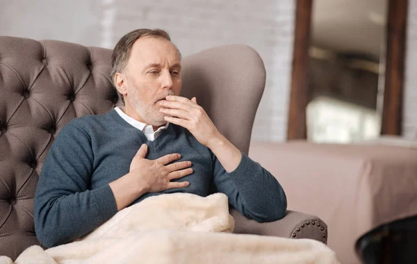 Viejo sentado en el sofá y tosiendo — Foto de Stock