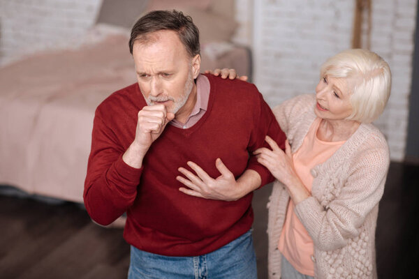 Мужчина в возрасте кашляет рядом со своей женой
