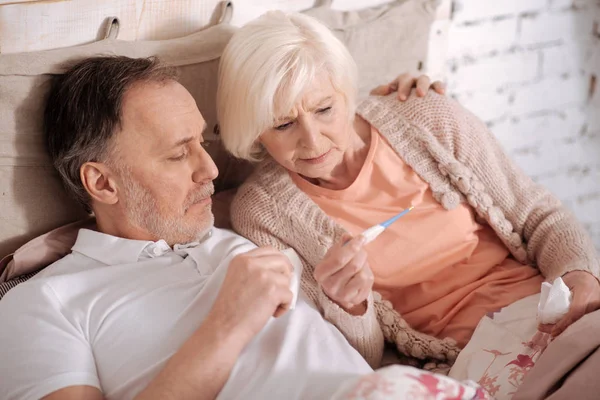 Senior couple lying on bed and checking thermamet — Stock Photo, Image