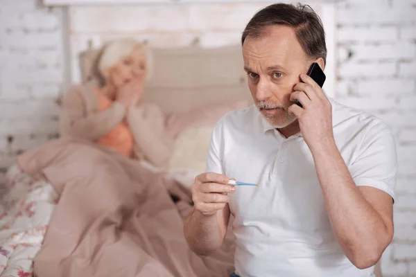 Hombre anciano con termómetro llamando a emergencias — Foto de Stock