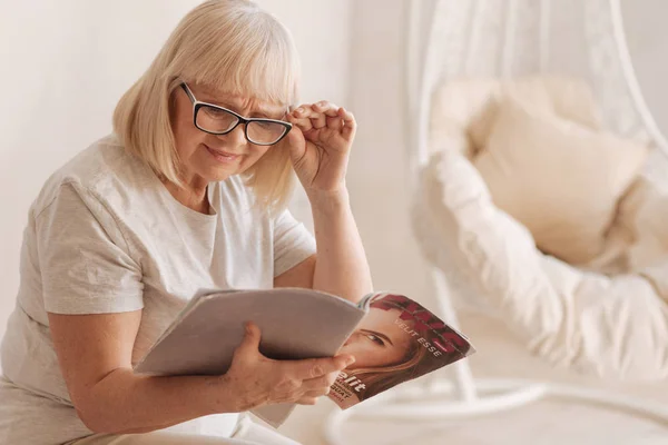 Mulher idosa agradável lendo uma revista de moda — Fotografia de Stock
