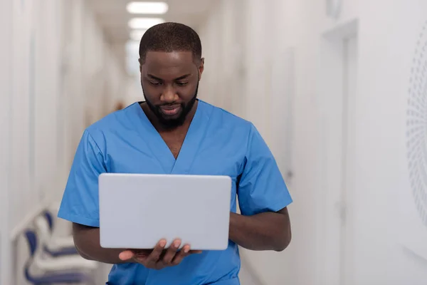 Médico afro-americano envolvido de pé e usando gadget no hospital — Fotografia de Stock