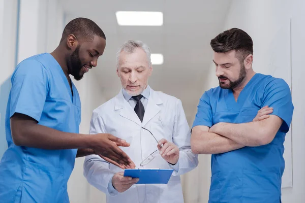 Un vieux médecin impliqué consulte de jeunes collègues au travail — Photo