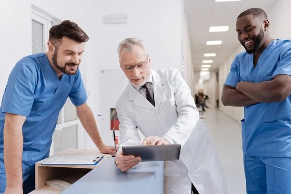 Bärtiger lächelnder Praktizierender genießt das Gespräch mit Kollegen bei der Arbeit — Stockfoto