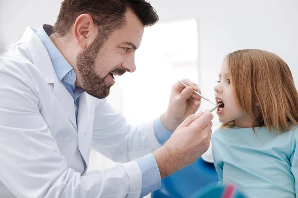 Нежный стоматолог-педиатр спрашивает своего пациента, открывая ей рот — стоковое фото