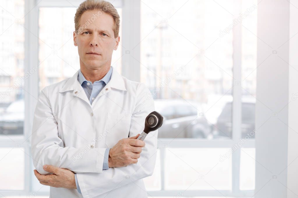 Confident aged dermatologist holding dermatoscope at work