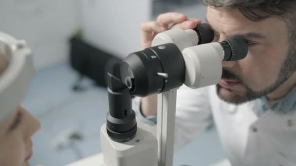 Optometrista masculino adulto medio que examina el ojo de los pacientes — Vídeos de Stock