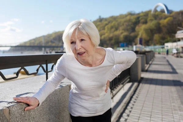 Suffering from back pain pensioner standing on the quay — Stock Photo, Image