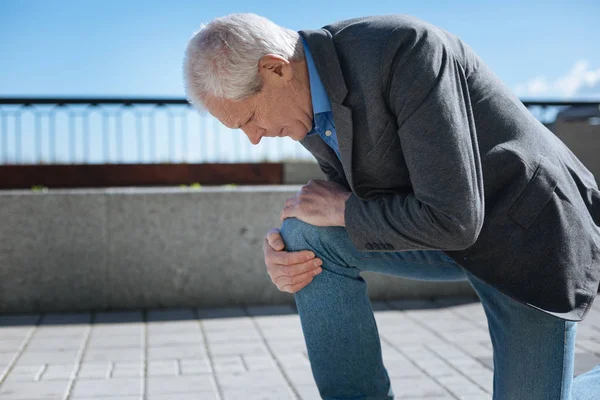 Pensionista concentrado sofrendo de dor de joelho no parque — Fotografia de Stock